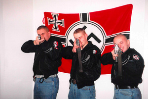Mitglieder der Hammerskins posieren bewaffnet vor einer Hakenkreuzfahne.